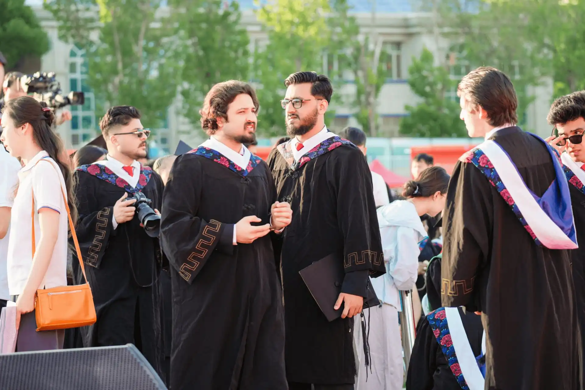Graduates in graduation gowns standing outdoors on campus