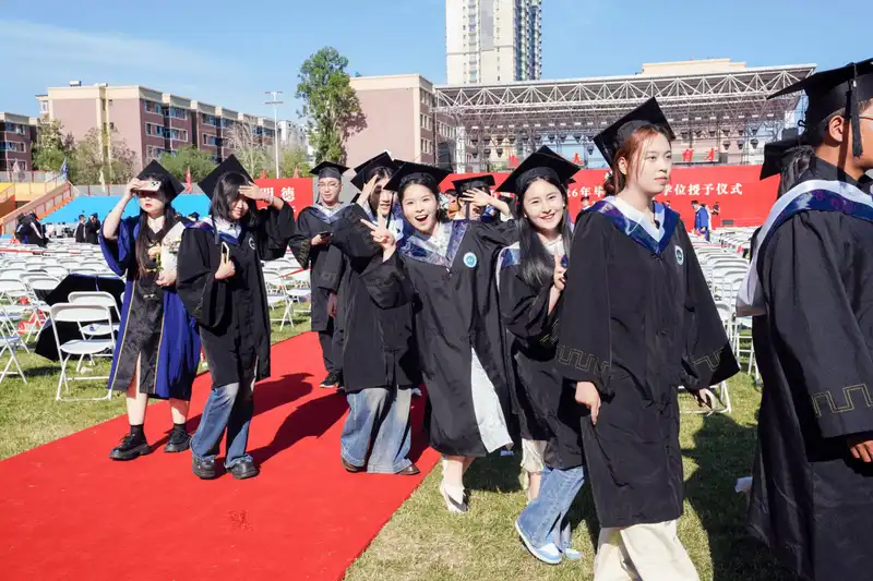 Graduates in academic gowns walking along red carpet outdoors