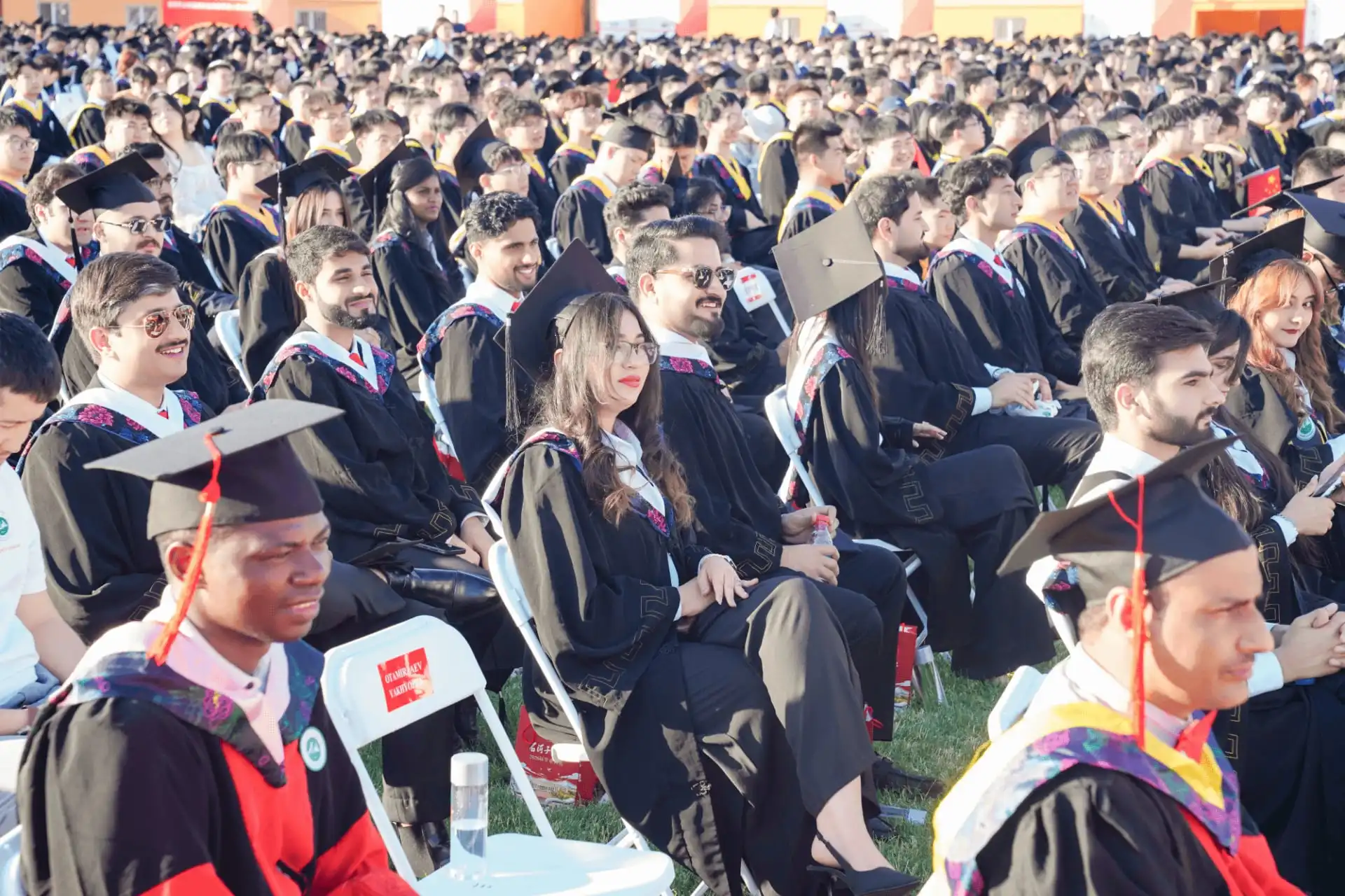 Large outdoor university graduation ceremony with seated students in academic gowns