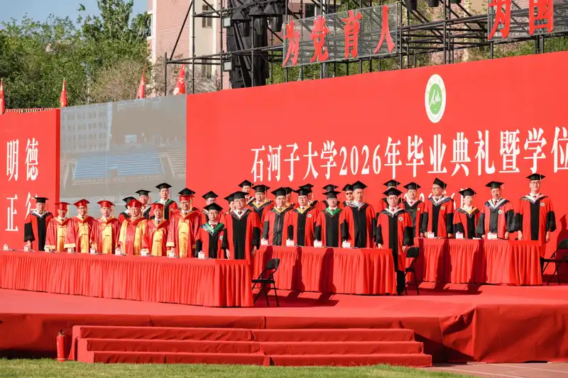 Large group of graduates gathered near stage at outdoor commencement
