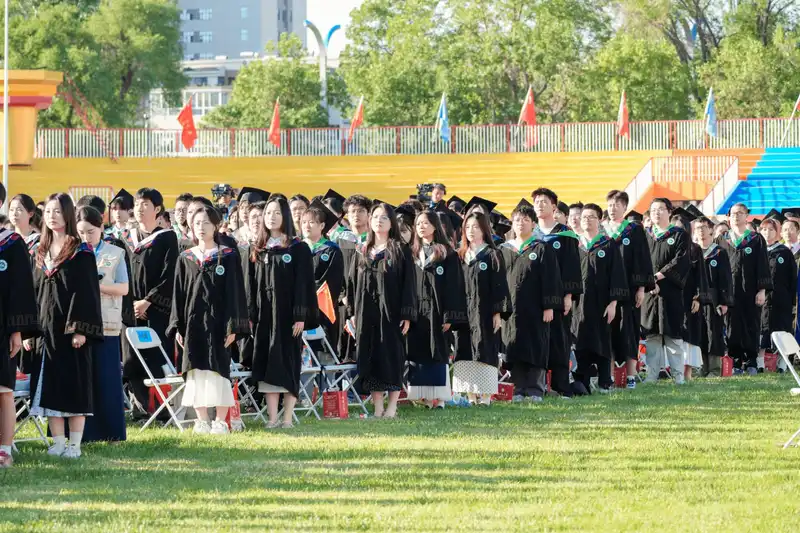 Graduates seated outdoors in rows during university graduation event