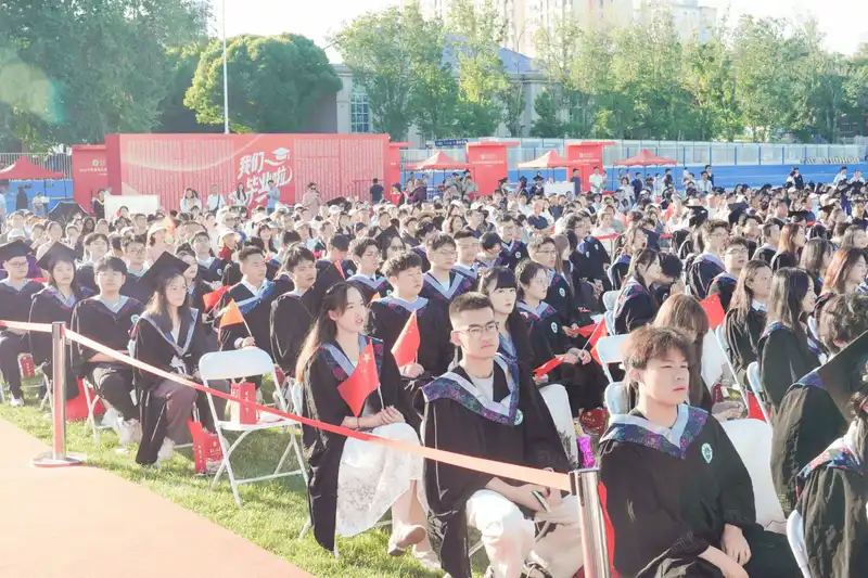 Graduates seated outdoors under clear sky at commencement ceremony