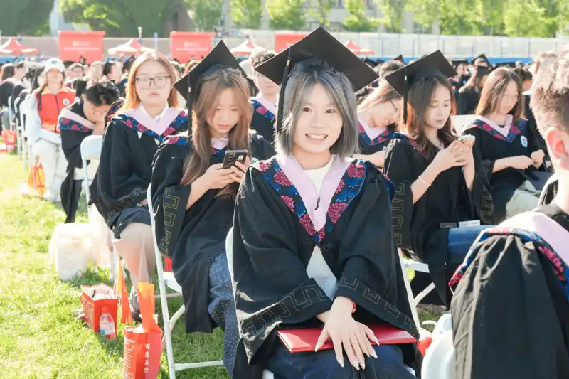 Graduates sitting outdoors wearing caps and gowns looking forward